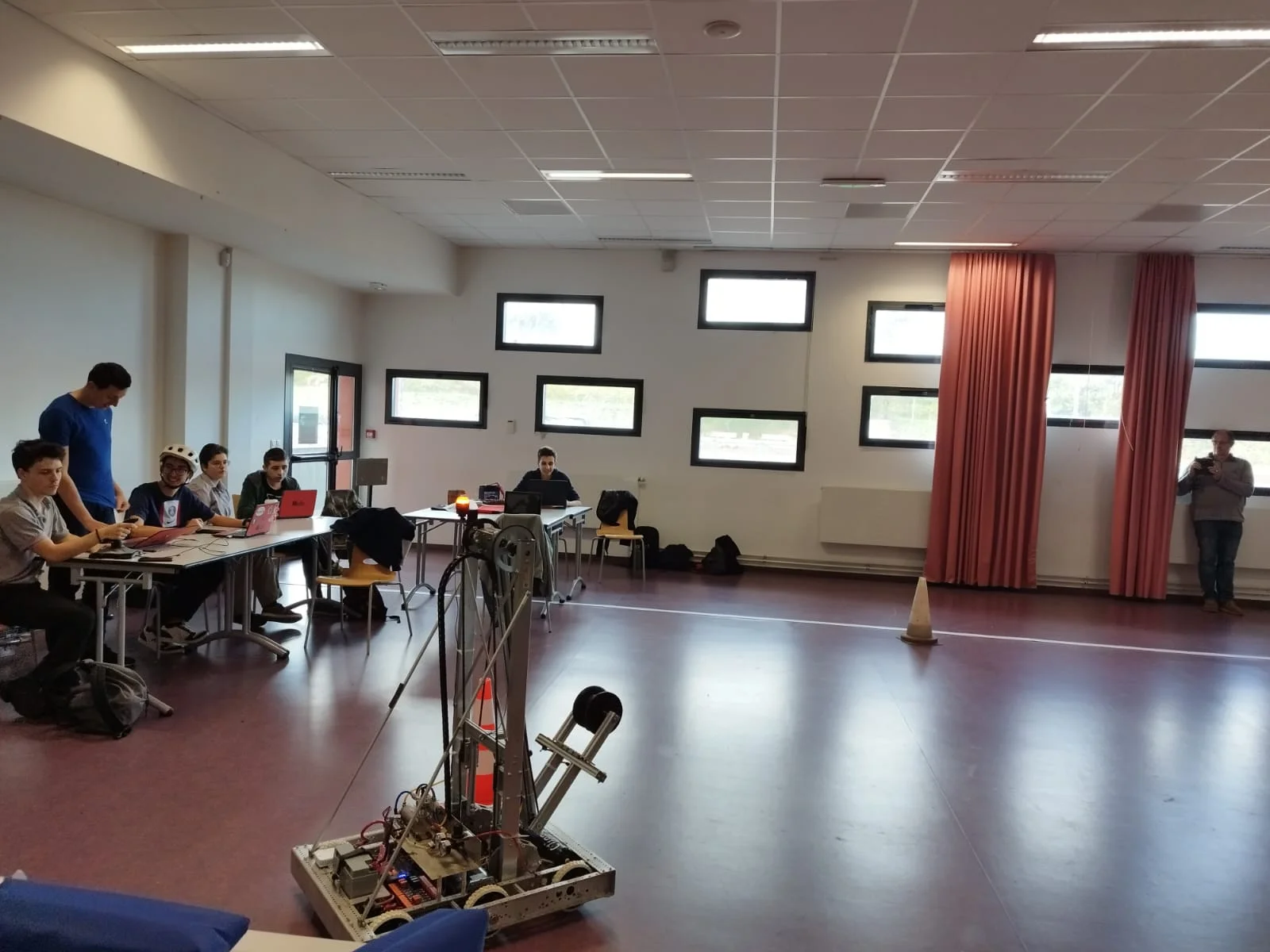 Dans une salle du lycée, le robot au premier plan et les membres de l’équipe réunis autour des ordinateurs.
